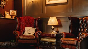 A traditional room with two leather armchairs, a small table with a lamp, and a fireplace. - Wheatacre White Lion (Beccles)