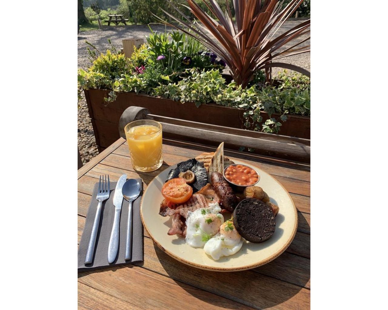 Uma mesa de madeira com um prato de comida de café da manhã, incluindo ovos, bacon e feijão, e um copo de suco de laranja.