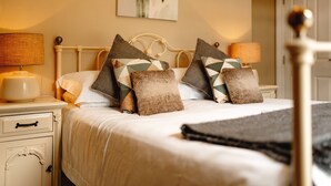 A neatly made bed with patterned pillows, a bedside table with a lamp, and a wall-mounted painting. - Wheatacre White Lion (Beccles)