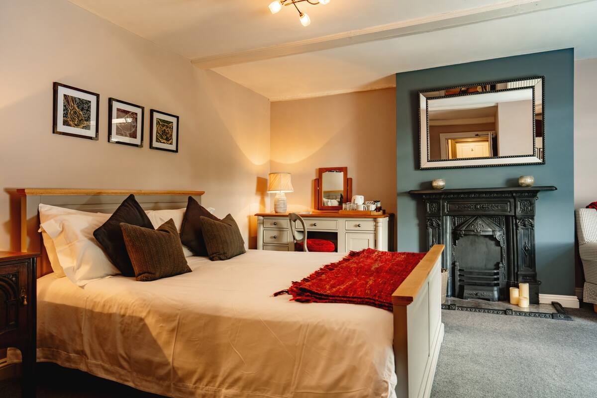 A neatly arranged bedroom with a large bed, a dresser, a mirror, and a fireplace.