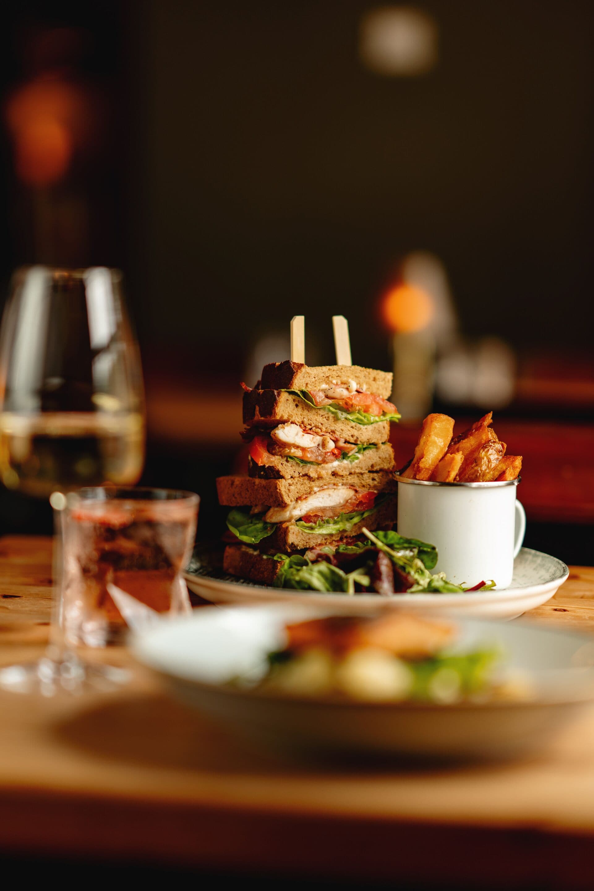 Un montón de sándwiches con palillos, una pequeña porción de papas fritas y un vaso de bebida sobre una mesa de madera.