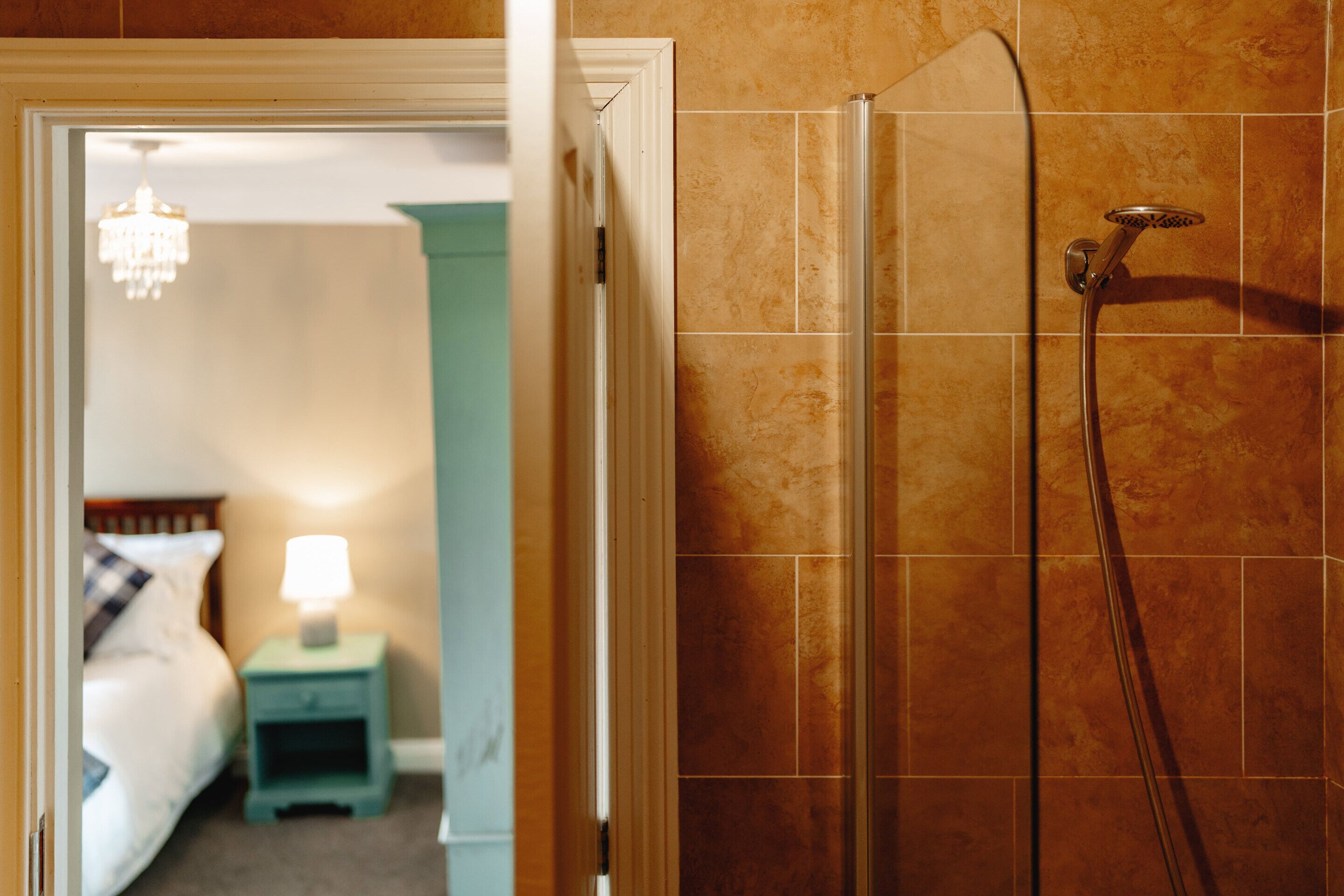 Een badkamer met een douche, een bed en een nachtkastje met een lamp.