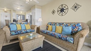 A living room with wicker furniture, a ceiling fan, and decorative wall art. - Las Palmas 224 2 Bedroom Condo by RedAwning (Gulf Shores)