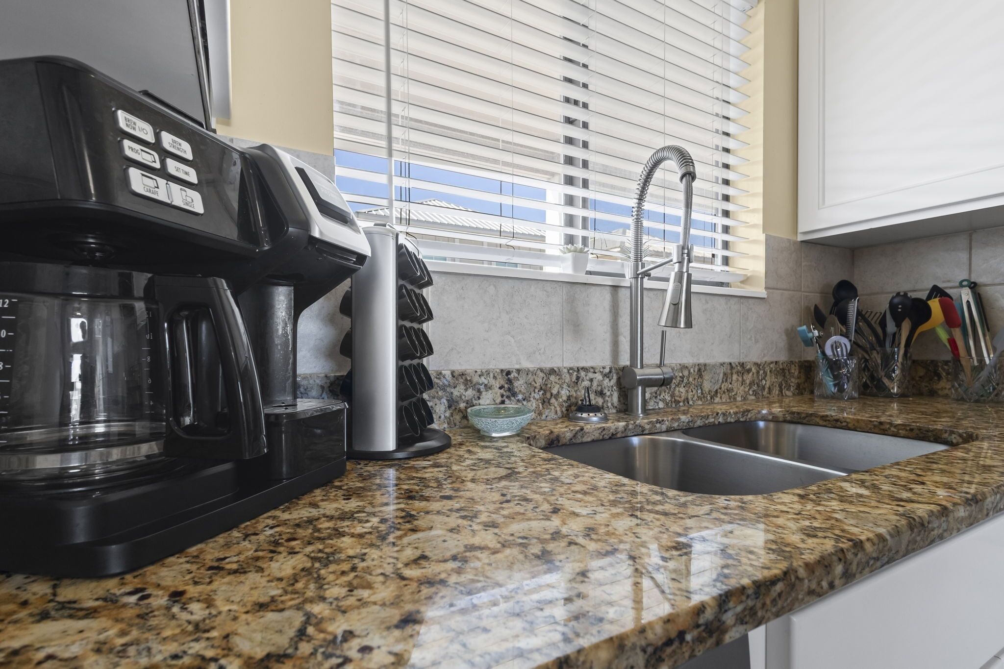 A kitchen with a coffee maker, a sink, and a window with blinds.