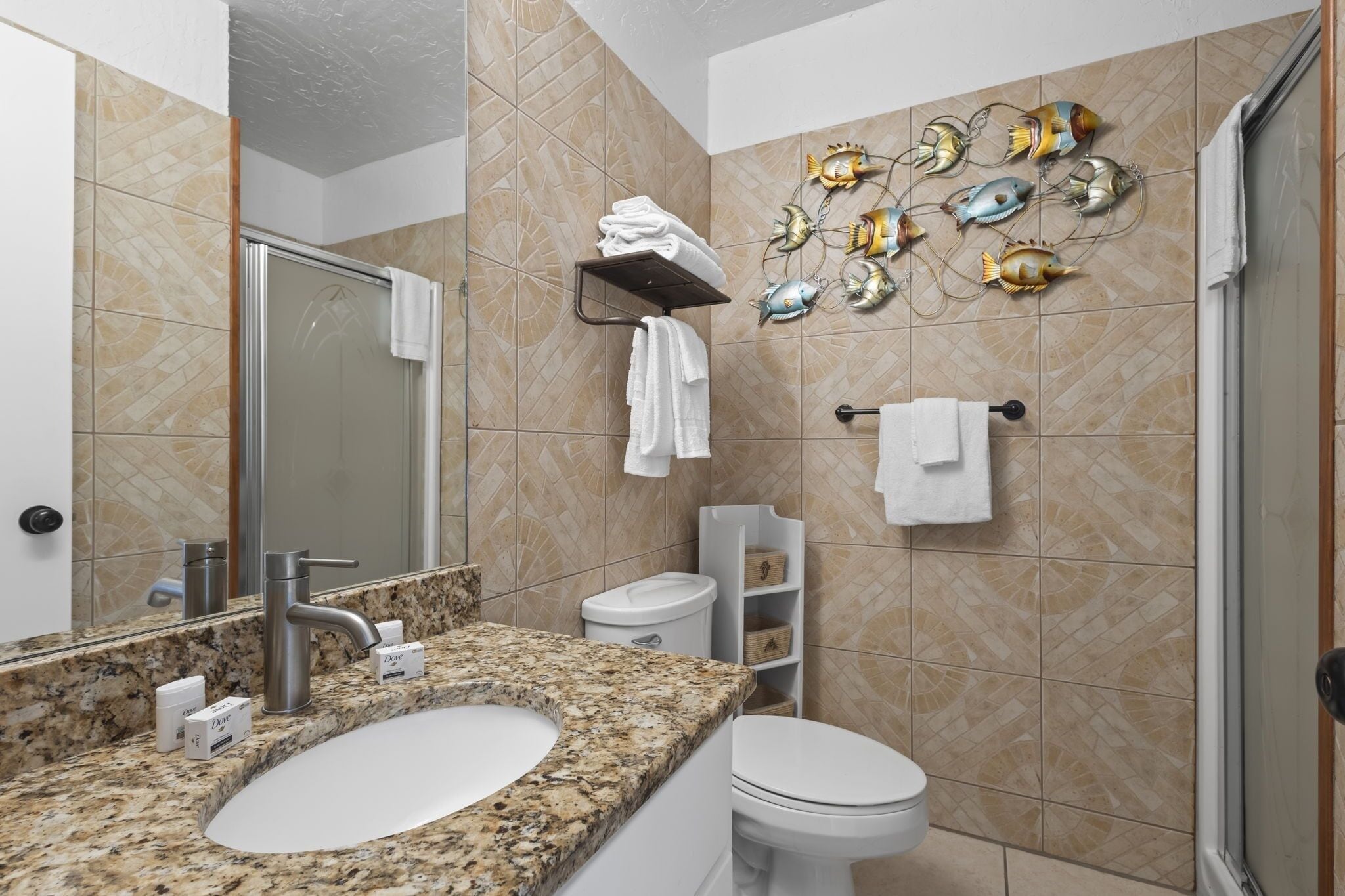 Baño con lavamanos de encimera de granito, inodoro blanco y zona de ducha.