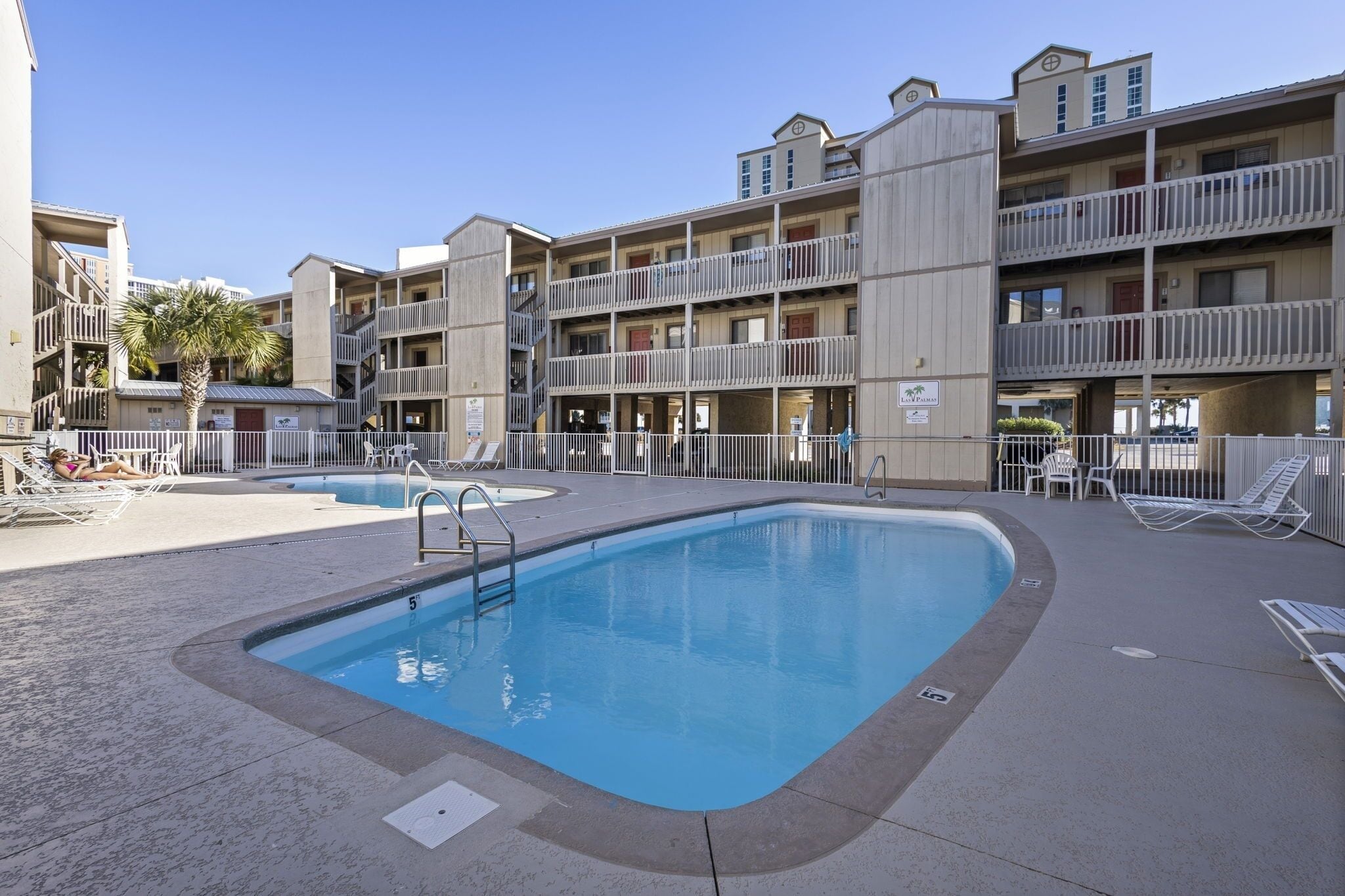 A pool area with lounge chairs and a building with balconies.