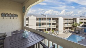 A balcony with a view of a hotel building, a pool, and a sign that reads "BEACH". - Las Palmas 224 2 Bedroom Condo by RedAwning (Gulf Shores)