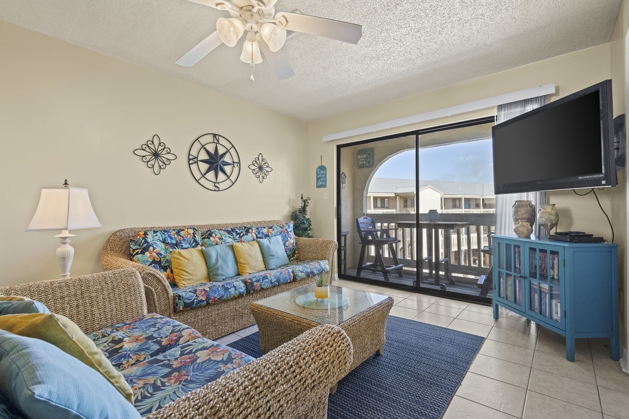 A living room with wicker furniture, a flat-screen TV, and a balcony with a view.