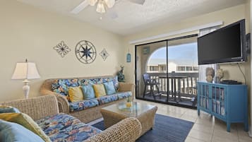 A living room with wicker furniture, a flat-screen TV, and a balcony with a view.
