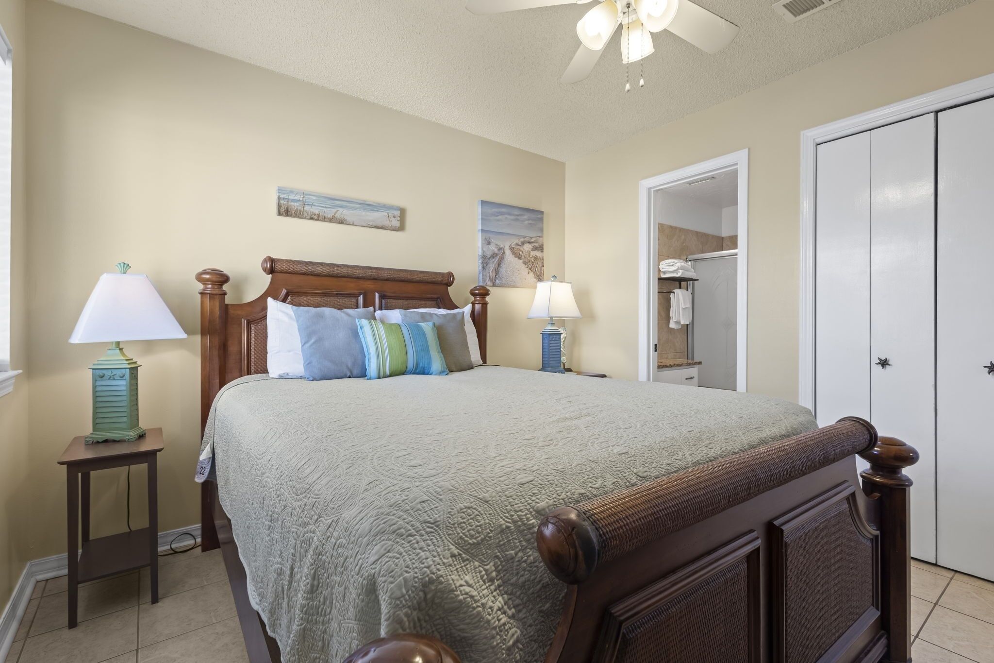 A bedroom with a bed, two bedside tables with lamps, a ceiling fan, and a wardrobe.
