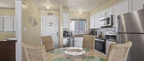 A modern kitchen with white cabinets, a stainless steel refrigerator, and a round table with woven chairs.