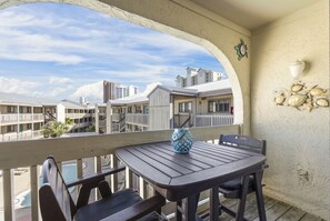 A balcony with a wooden table and chairs, a decorative vase, and a view of other buildings. - Las Palmas 224 2 Bedroom Condo by RedAwning (Gulf Shores)