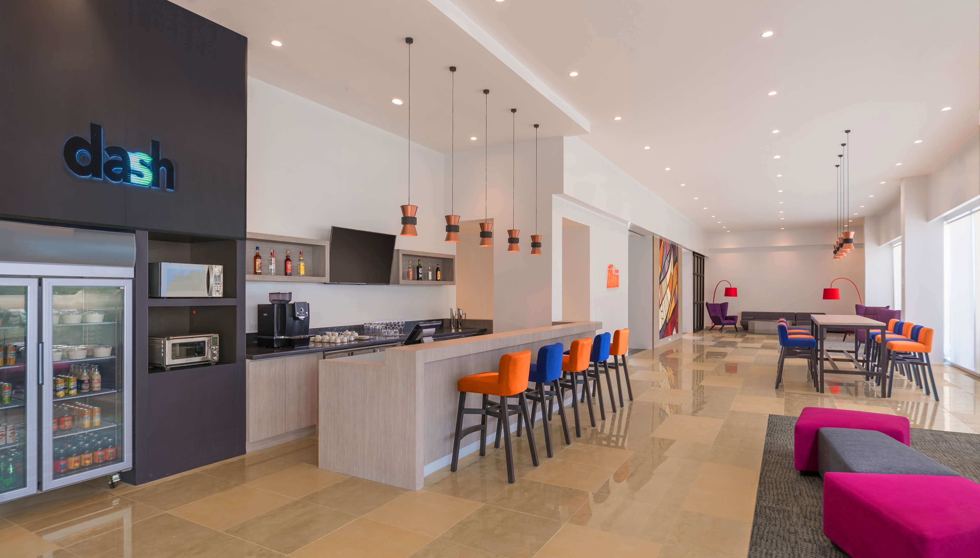 A modern hotel lobby with a bar area, seating, and a refrigerator stocked with beverages.