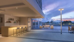 A modern outdoor bar area with seating and a view of the city skyline at dusk.