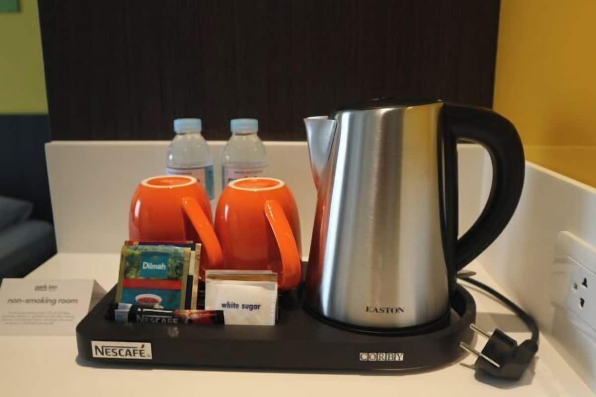 Eine Nescafé-Kaffeestation mit einer Edelstahl-Kaffeekanne, zwei orangenen Tassen, zwei Wasserflaschen, einer kleinen Packung Zucker und einem Schild, das auf einen Nichtraucherraum hinweist.