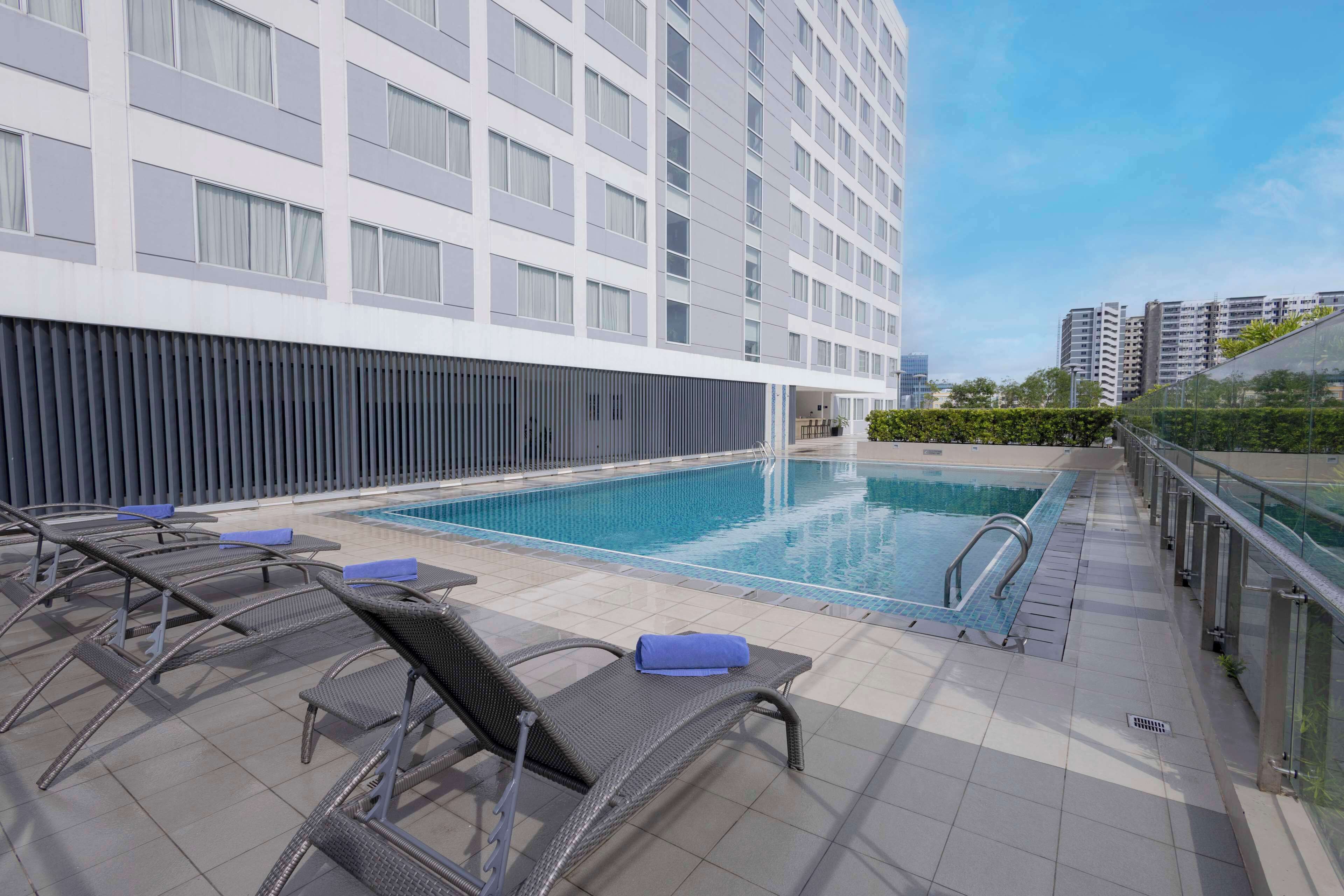 A rooftop swimming pool with lounge chairs and a modern building in the background.