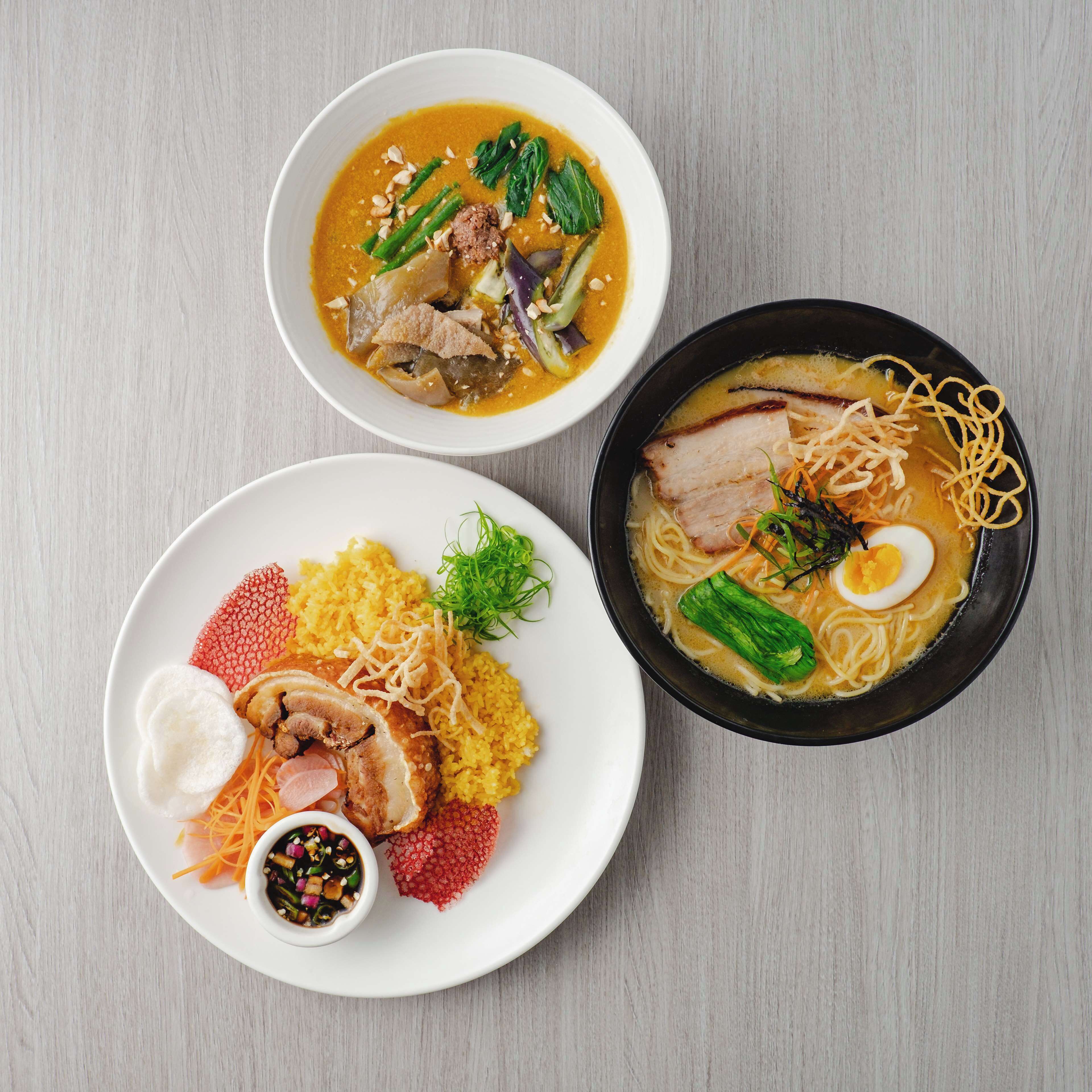 Drei Schüsseln mit asiatischer Nudelsuppe, verschiedene Beläge und Beilagen.