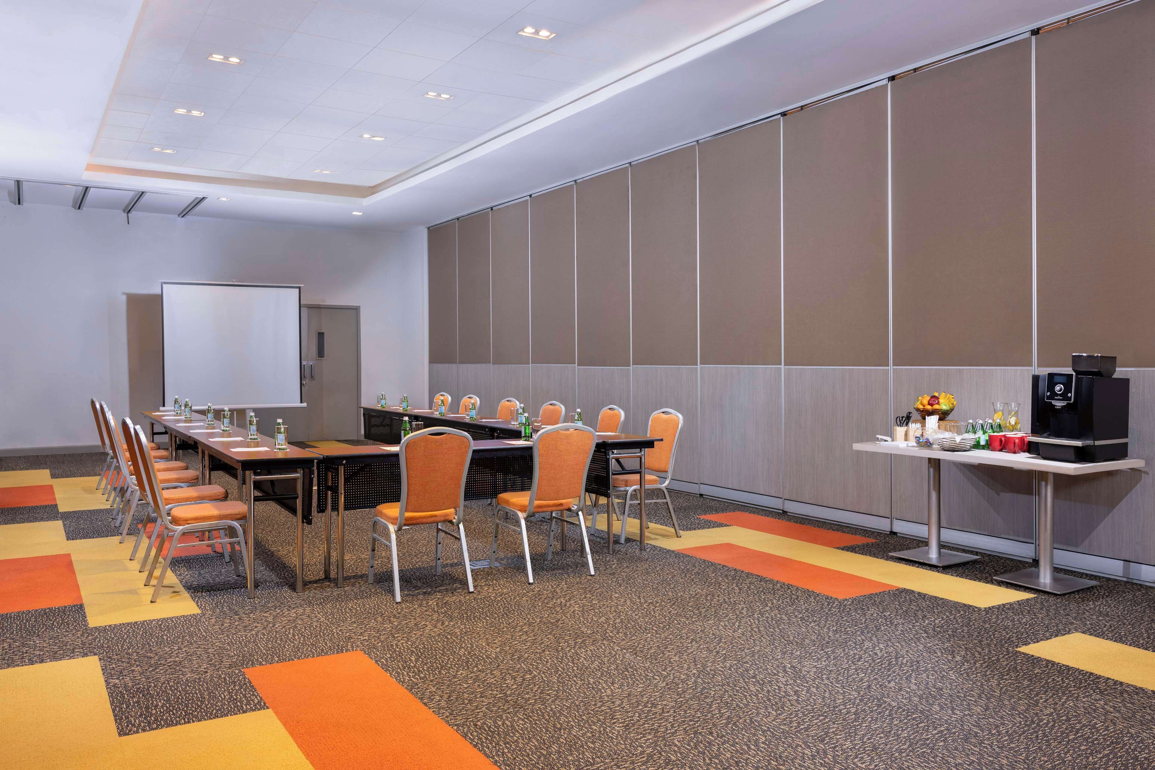 Un salón de conferencias con una mesa larga, sillas, una pantalla de proyector y una estación de café.