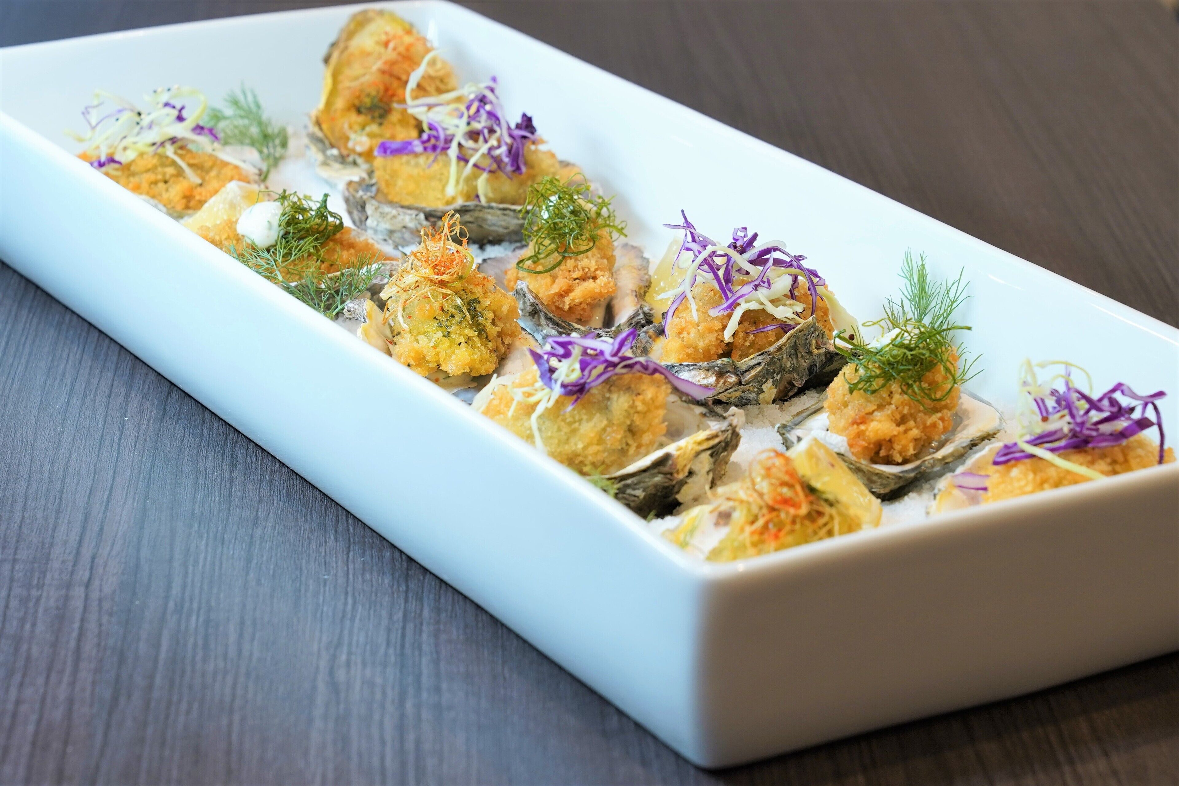 Un plato blanco rectangular con alimentos, decorado con hierbas moradas y verdes.