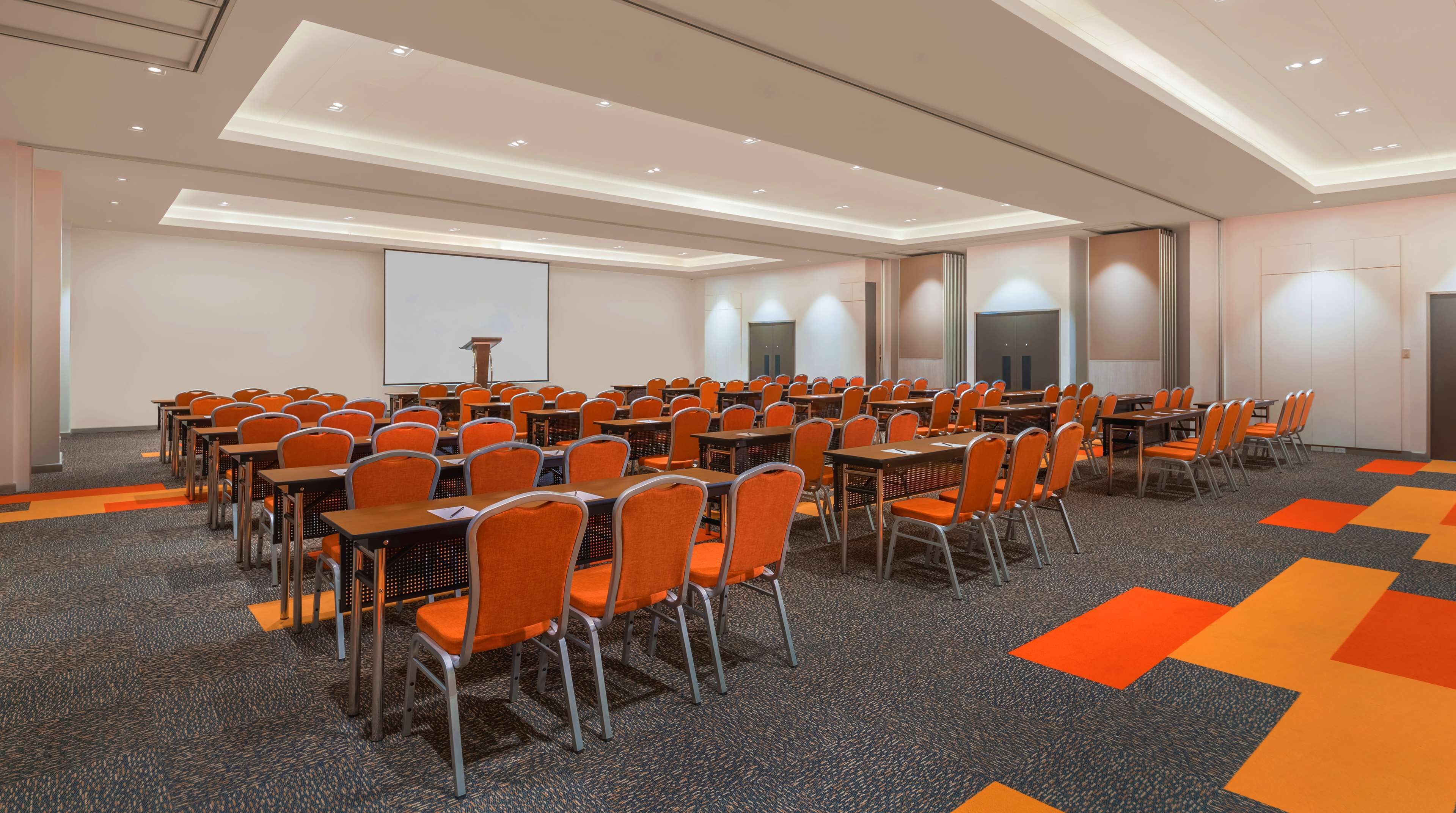 A conference room with rows of tables and chairs, a projector screen, and a podium.