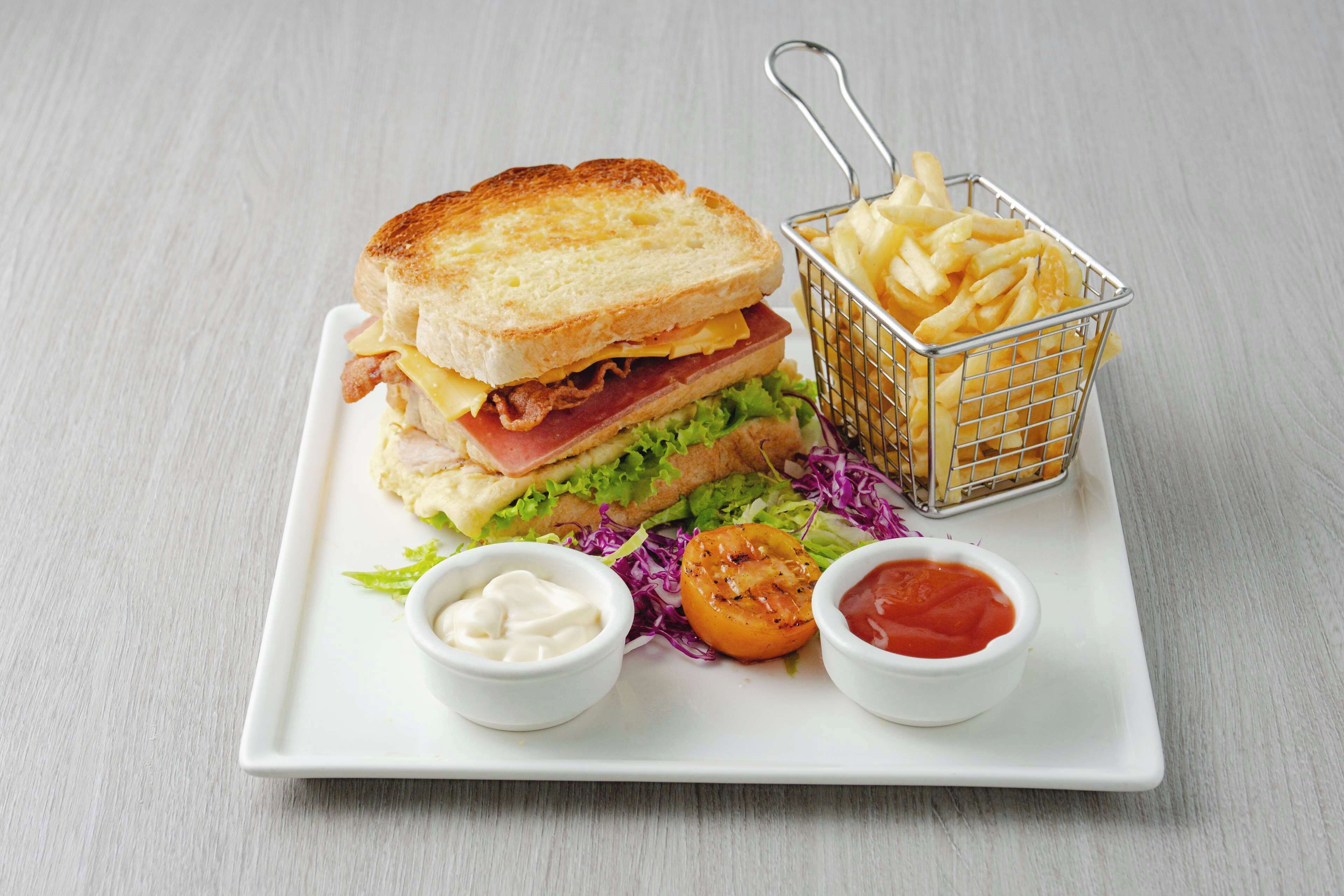 A sandwich with fries and two dipping sauces on a white plate.