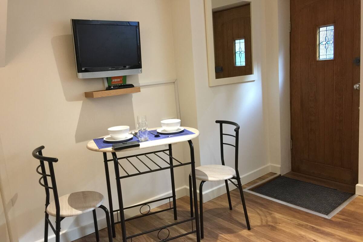 A small room with a TV mounted on the wall, a wooden door with a window, and a table with chairs.