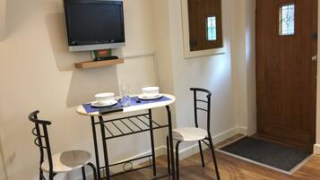 A small room with a TV mounted on the wall, a wooden door with a window, and a table with chairs.