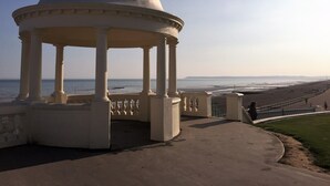 A white gazebo with a dome roof, columns, and a balustrade, overlooking a beach and the ocean.