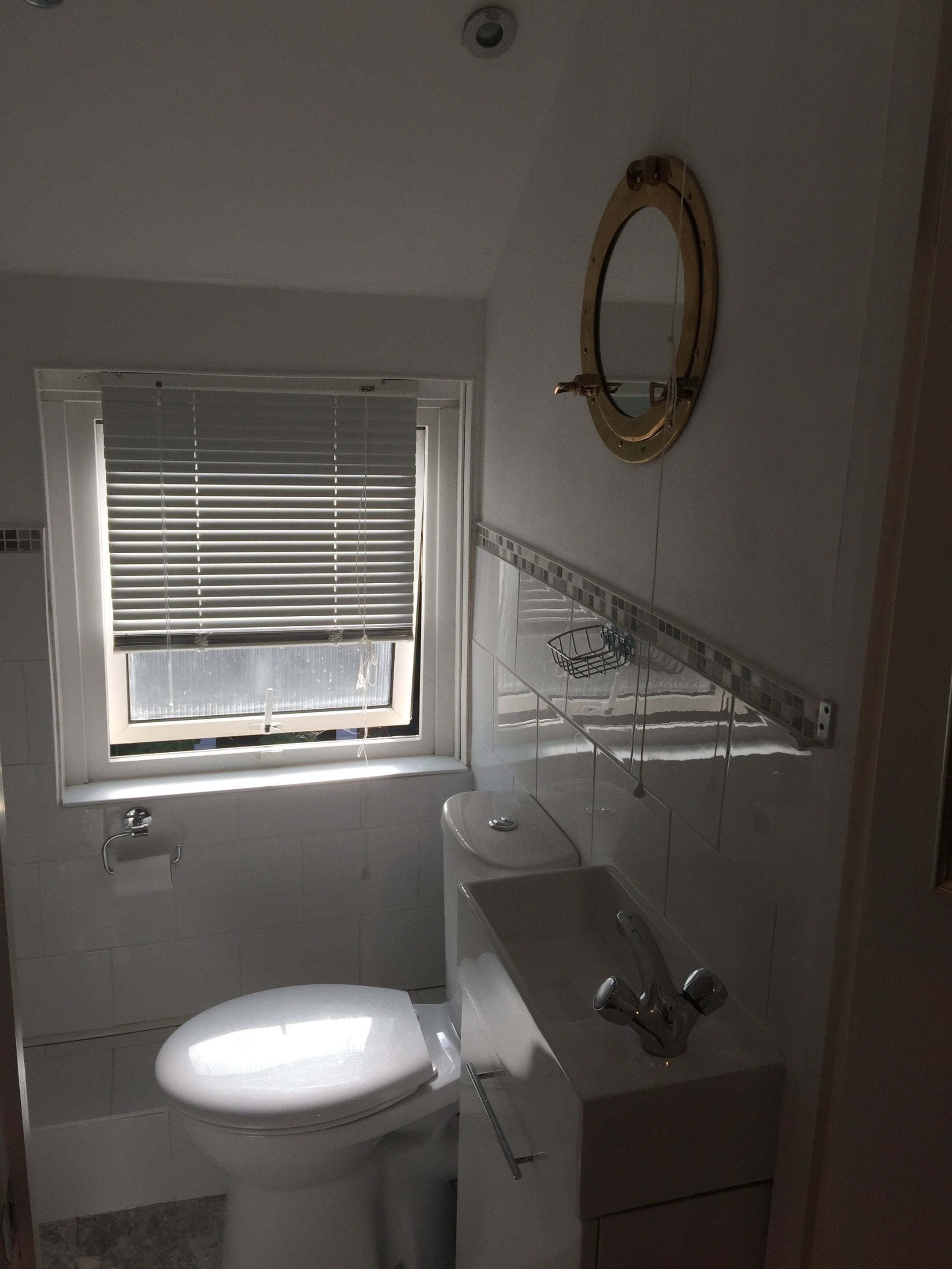 A bathroom with a toilet, sink, and window with blinds.