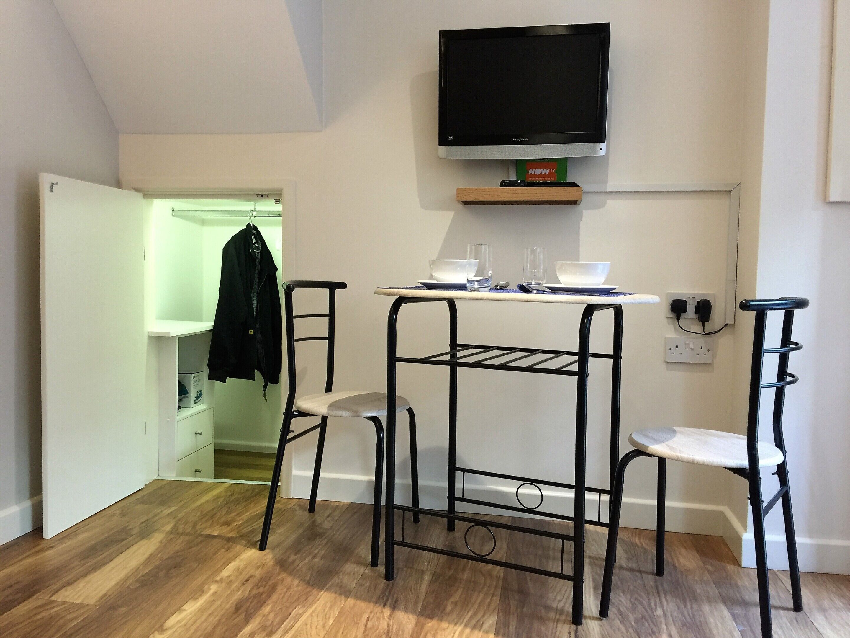 A compact kitchen with a TV, a small table, and two chairs.