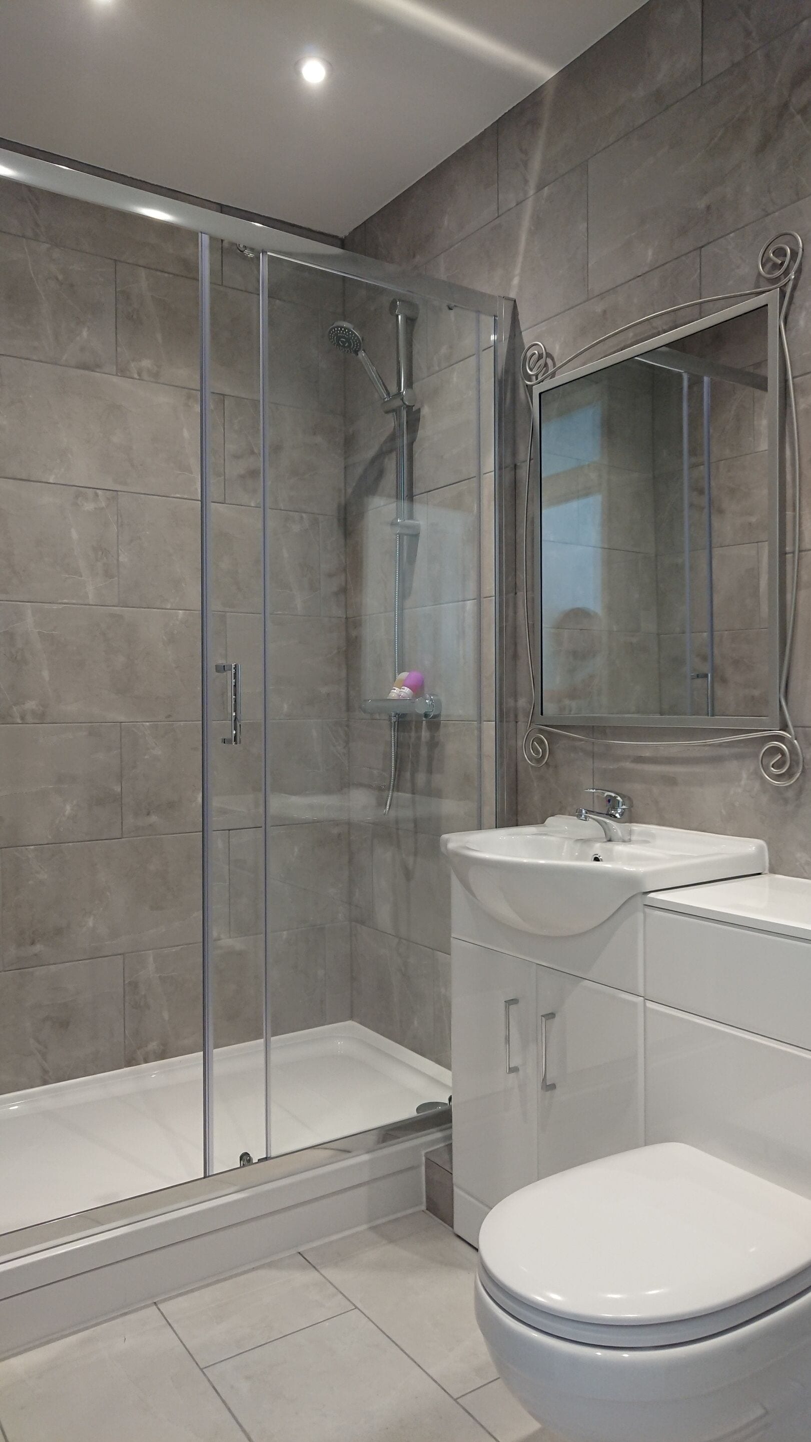 A modern bathroom with a glass-enclosed shower, a white sink, and a toilet.