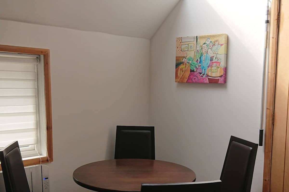 A dining area with a round table and four chairs, a skylight, a painting on the wall, and a door.