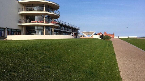 A modern building with a curved facade, multiple balconies, and a grassy area in front.