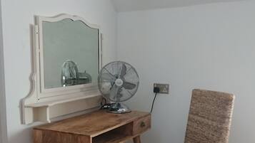 A room with a wooden desk, a wicker chair, a standing fan, and a mirror.
