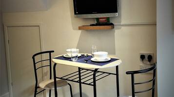 A small dining area with a table and two chairs, a television mounted on the wall, and a door in the background.