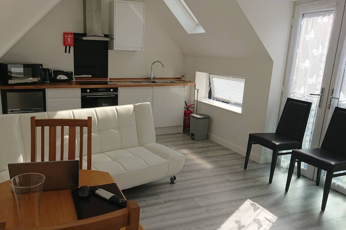 A compact living space with a kitchenette, a sofa, a dining table, and a window with blinds.