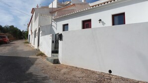 Un bâtiment blanc avec des portes rouges et une petite fenêtre. Une voiture est garée sur le côté gauche de la route.