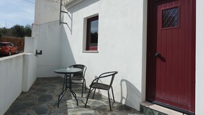 Une petite terrasse extérieure avec une table et deux chaises, une porte rouge et une fenêtre.