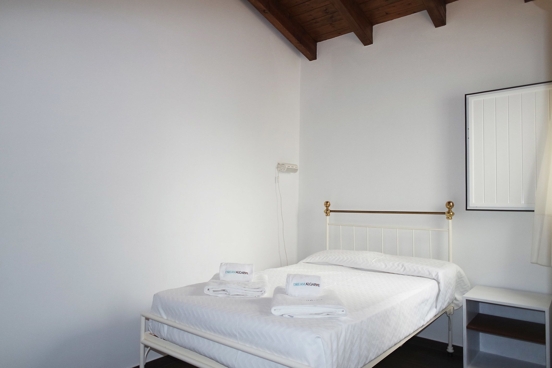A white bed with a brass headboard, a white bedside table, and a white wall with a white door.