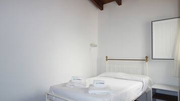 A white bed with a brass headboard, a white bedside table, and a white wall with a white door.