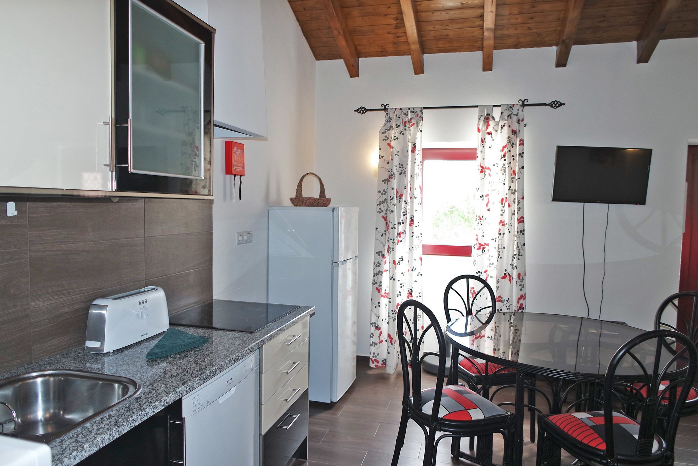 Una cocina equipada con tostadora, refrigerador y pileta. Hay una mesa de comedor con sillas y un televisor montado en la pared.