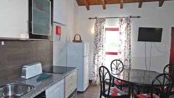Una cocina equipada con tostadora, refrigerador y pileta. Hay una mesa de comedor con sillas y un televisor montado en la pared.