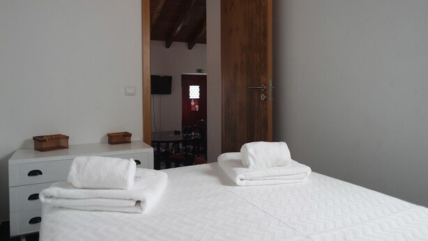 Une chambre d’hôtel avec deux lits, une porte en bois, une commode blanche et une petite table sur laquelle sont posés deux paniers.