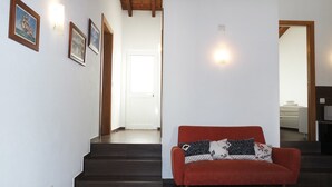 Un escalier menant à une porte, un canapé rouge orné de coussins à motifs et des tableaux encadrés accrochés au mur.
