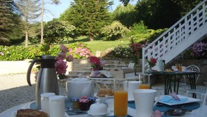 An outdoor breakfast setup with a table, breakfast items, and a staircase leading to a higher level. - B&B Le Clos Saint-Jean - Omaha Beach (Aure sur Mer)