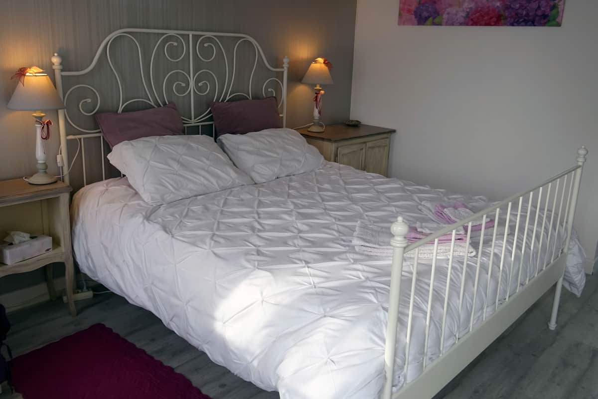A neatly made bed with a white quilt, two bedside tables with lamps, and a floral painting on the wall.