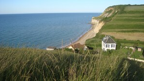 A coastal landscape with a beach, grassy fields, and a house with a sloped roof. - B&B Le Clos Saint-Jean - Omaha Beach (Aure sur Mer)