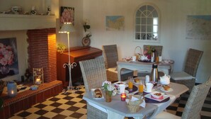 A dining area with checkered flooring, wicker furniture, and a table set for breakfast with pastries, coffee, and a candle. - B&B Le Clos Saint-Jean - Omaha Beach (Aure sur Mer)