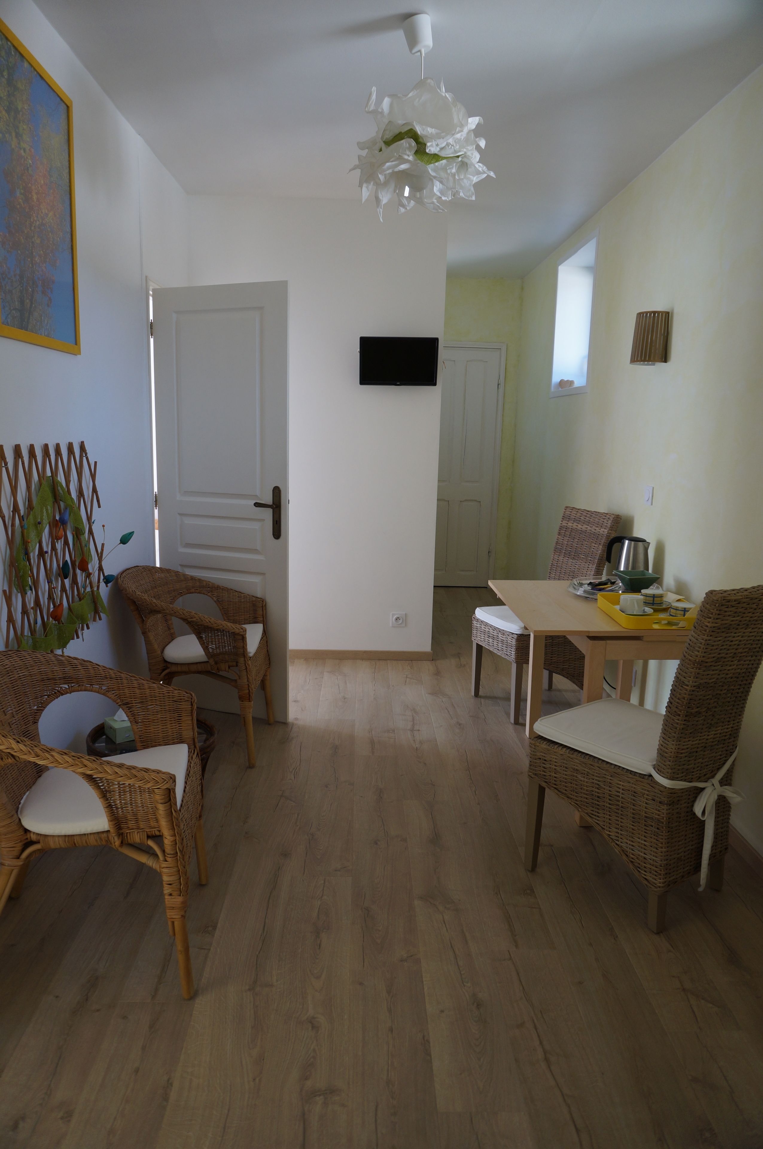 Un comedor con sillas de mimbre y una mesa, una puerta blanca y una lámpara en el techo.