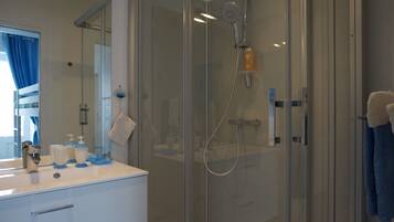 Een moderne badkamer met een douchecabine van glas, een witte wastafel met blauwe zeepdispensers, en een spiegel met een blauw gordijn.